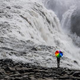 tosender Wasserfall mit Person mit einem regenbogenfarbigen Schirm