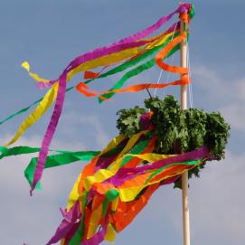 Aufgerichtete Holzstange mit grünem Kranz und farbigen Bänder.